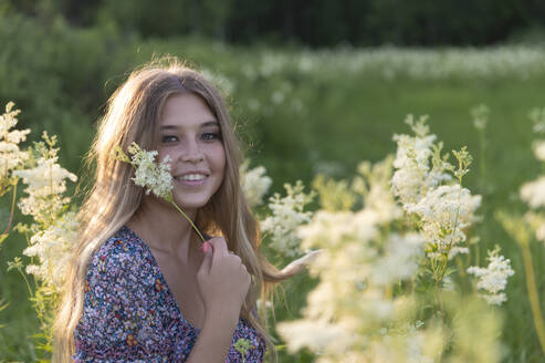 Glückliche junge Frau mit Blumen auf einem Feld bei Sonnenuntergang - VBUF00274