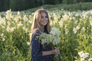 Smiling young woman holding bouquet of flowers standing in field - VBUF00275