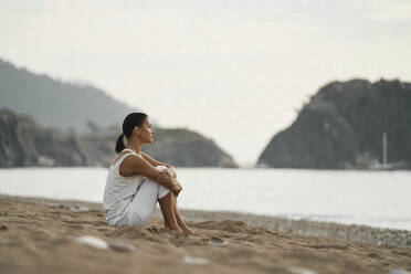 Thoughtful woman sitting on sand at beach - ANNF00033