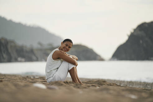 Happy woman sitting on sand at beach - ANNF00034