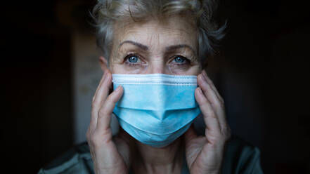Depressed senior woman with face mask standing in bathroom at home, coronavirus and mental health concept. - HPIF07986