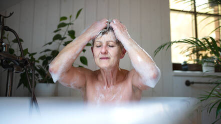 Porträt einer zufriedenen älteren Frau, die sich zu Hause in einer Badewanne mit Schaumbad wäscht, die Augen geschlossen. - HPIF07996