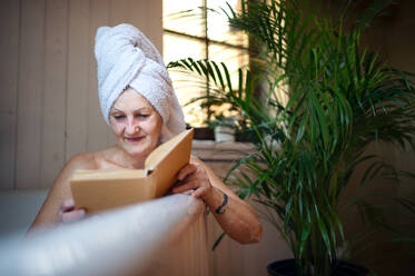 A happy senior woman reading book in bath tub at home. - HPIF07998