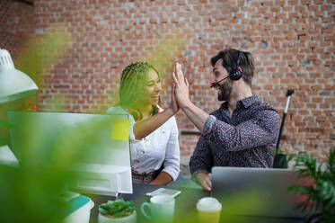 Fröhliche junge Geschäftsleute sitzen und arbeiten am Schreibtisch im Büro, ein Konzept der Zusammenarbeit. - HPIF08006