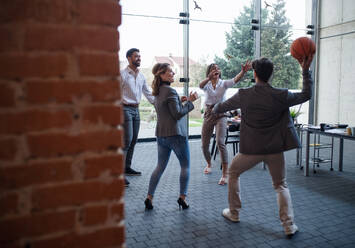 Eine Gruppe fröhlicher junger Geschäftsleute spielt Basketball im Büro und macht eine Pause. - HPIF08017