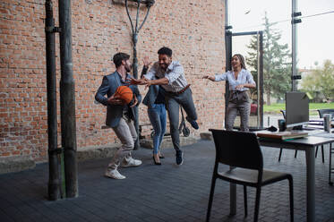 Eine Gruppe fröhlicher junger Geschäftsleute spielt Basketball im Büro und macht eine Pause. - HPIF08018