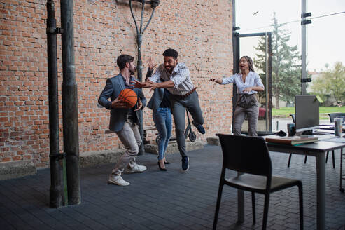 Eine Gruppe fröhlicher junger Geschäftsleute spielt Basketball im Büro und macht eine Pause. - HPIF08018