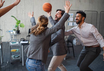 A group of cheerful young businesspeople playing basketball in office, taking a break concept. - HPIF08019