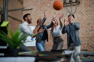 Eine Gruppe fröhlicher junger Geschäftsleute spielt Basketball im Büro und macht eine Pause. - HPIF08022