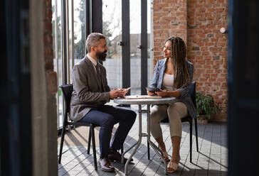 A portrait of businesspeople sitting at the table and working indoors, discussing issues. - HPIF08062