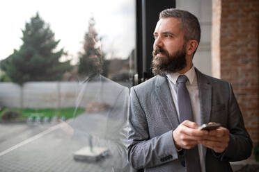 A portrait of mature businessman standing indoors, using smartphone. - HPIF08064