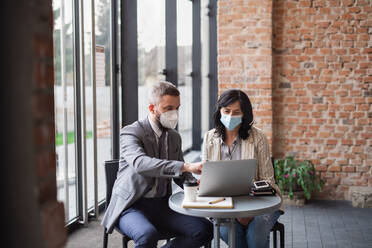 A portrait of businesspeople sitting at the table and working indoors, coronavirus concept. - HPIF08068