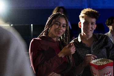 Fröhliches junges Paar, das Popcorn isst, während es sich einen Film im Kino ansieht und in die Kamera schaut. - HPIF08121