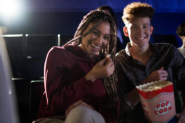 Fröhliches junges Paar, das Popcorn isst und lachend einen Film im Kino ansieht. - HPIF08122