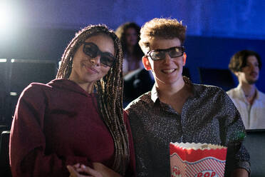 Junges Paar mit 3D-Brille und Popcorn, das sich im Kino einen Film ansieht und in die Kamera schaut. - HPIF08123