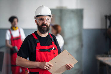 Ein Porträt eines Arbeiters mit Helm und Schutzbrille in einer Fabrik, der in die Kamera schaut. - HPIF08126