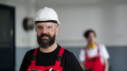 Ein Porträt eines Arbeiters mit Helm und Schutzbrille in einer Fabrik, der in die Kamera schaut. - HPIF08127