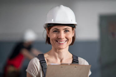 A low-angle view of worker with helmet indoors in factory looking at camera. - HPIF08130