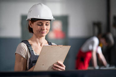 Tiefblick auf einen Arbeiter mit Helm und Klemmbrett in einer Fabrik, der ein Klemmbrett hält und arbeitet. - HPIF08131