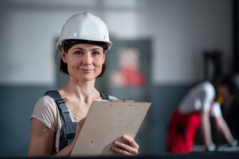 Blick aus geringer Höhe auf einen Arbeiter mit Helm in einer Fabrik, der ein Klemmbrett hält. - HPIF08132
