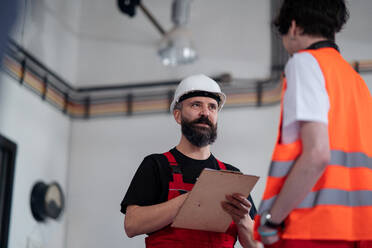 Porträt von männlichen Arbeitern mit Helm, die in einer Fabrik arbeiten und sich über Probleme unterhalten. - HPIF08137