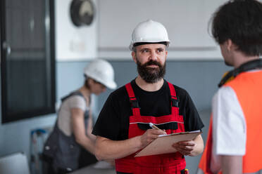 Porträt von männlichen Arbeitern mit Helm, die in einer Fabrik arbeiten und sich über Probleme unterhalten. - HPIF08139