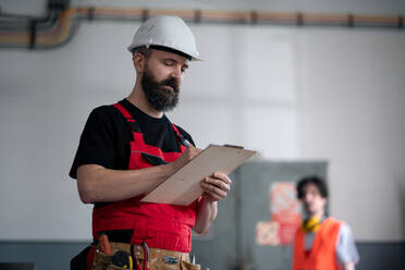 Ein männlicher Arbeiter mit Helm in einer Fabrik, der ein Klemmbrett hält. - HPIF08141