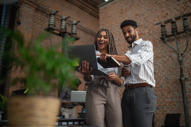 Cheerful young businesspeople with laptop working in office, a cooperation concept. - HPIF08178