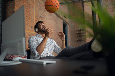 A cheerful young businessman with headphones and ball taking a break in office, resting. - HPIF08190