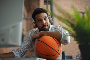 A cheerful young businessman with headphones and ball taking a break in office, resting. - HPIF08191