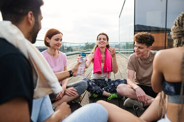 A group of young people talking and sitting in circle after exercise outdoors on terrace, sport and healthy lifestyle concept. - HPIF08231