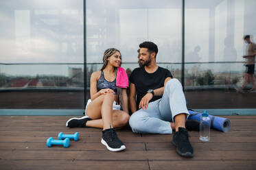 A young couple in love resting after exercise outdoors on terrace, sport and healthy lifestyle concept. - HPIF08242