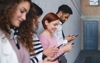 Seitenansicht einer Gruppe von Unternehmern, die in einem Büro an einer Betonwand stehen und ein Smartphone benutzen. - HPIF08258