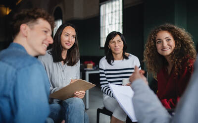 Ein Berater mit Männern und Frauen, die während einer Gruppentherapie im Kreis sitzen und sich unterhalten. - HPIF08269