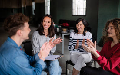 Fröhliche Männer und Frauen sitzen während einer Gruppentherapie im Kreis, reden und klatschen. - HPIF08270