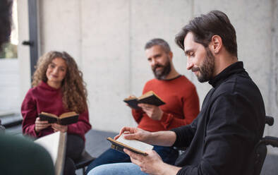 Männer und Frauen, die während einer Gruppentherapie im Kreis sitzen und ein Bibelbuch lesen. - HPIF08273