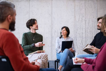 Ein Berater mit Männern und Frauen, die während einer Gruppentherapie im Kreis sitzen und sich unterhalten. - HPIF08276