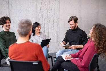 Glückliche Männer und Frauen, die während einer Gruppentherapie im Kreis sitzen, lesen und reden. - HPIF08277
