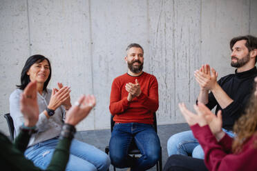 Joyful men and women sitting in circle during a group therapy, talking and clapping. - HPIF08282