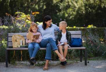Eine glückliche ältere Frau mit Enkelkindern sitzt auf einer Bank und hilft bei den Hausaufgaben im Park. - HPIF08290