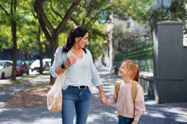 A happy grandmother taking granddaughter home from school, walking outdoors in street. - HPIF08298