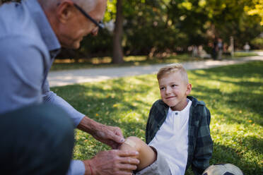 A little boy with injured leg getting plaster from grandfather outdoors in park. - HPIF08305