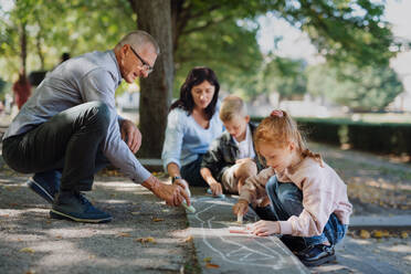 Ein älteres Ehepaar mit Enkelkindern zeichnet mit Kreide auf dem Bürgersteig im Park. - HPIF08306