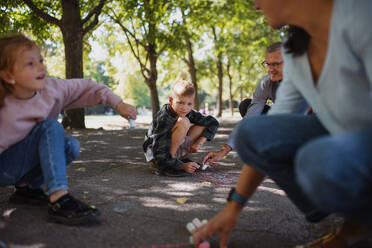 Ein älteres Ehepaar mit Enkelkindern zeichnet mit Kreide auf dem Bürgersteig im Park. - HPIF08307