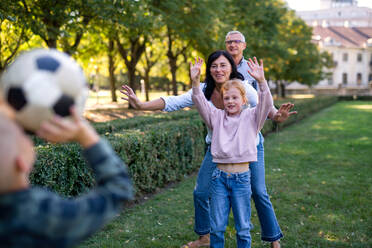 Happy little children with grandparents playing with a football outdoors in park - HPIF08311