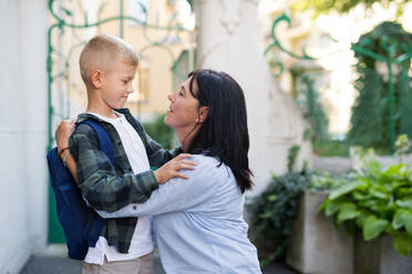 A happy schoolboy hugging his grandmother waiting for him after school outdoors in street. - HPIF08313