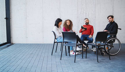 Sad and frustrated men and women in wheelchair sitting in circle during group therapy, reading and talking. - HPIF08315