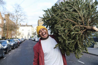 Fröhlicher Mann mit Weihnachtsbaum auf der Straße - ASGF03446