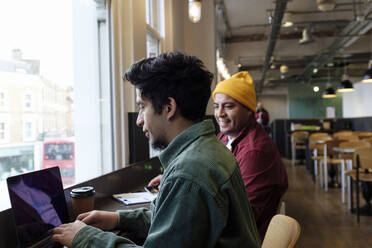 Junger Freiberufler arbeitet mit seinem Bruder in einem Café am Laptop - ASGF03454