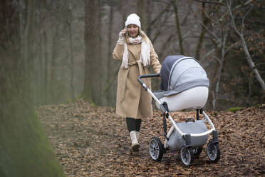 Frau mit Kinderwagen telefoniert mit Smartphone im Wald - NJAF00275